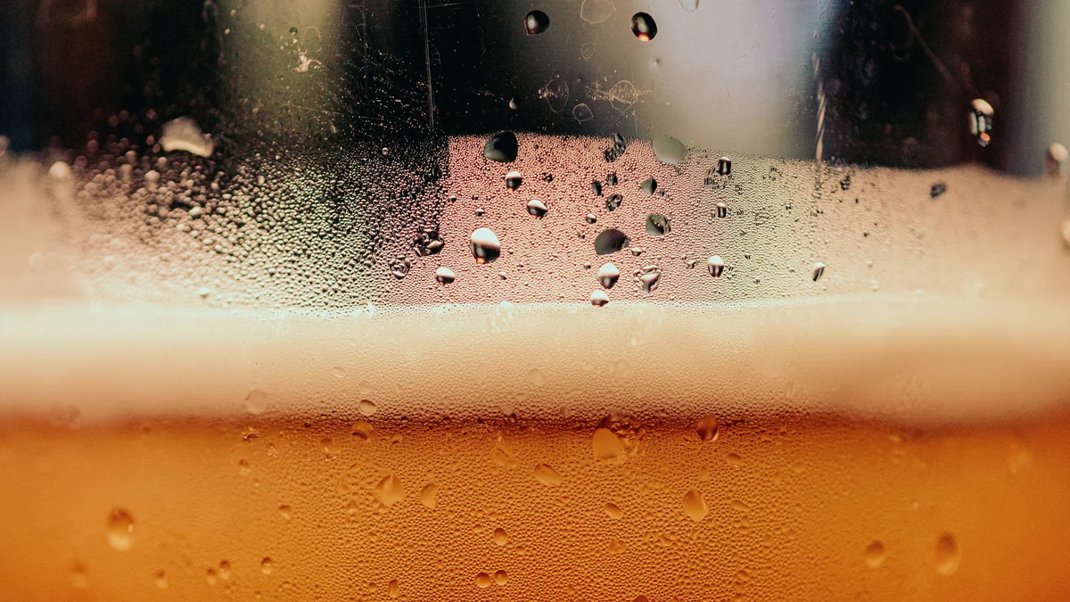 Espuma de un vaso de cerveza con gotas de condensación en el cristal