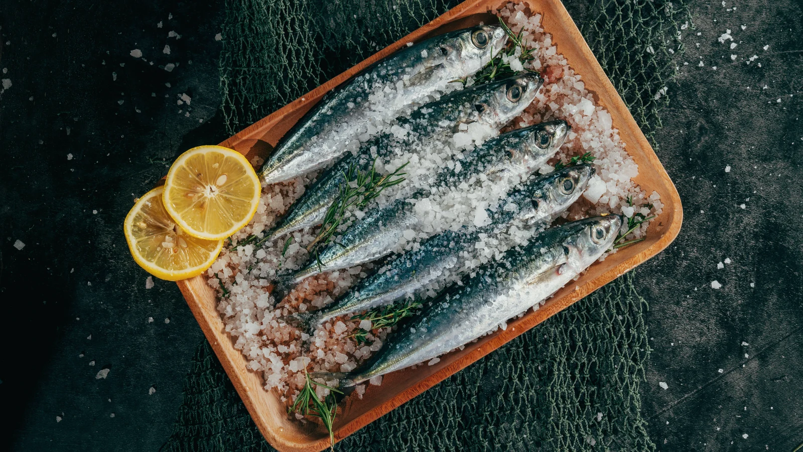 Alimentos con omega 3: sardinas frescas sobre sal gruesa en una bandeja de madera, con medio limón