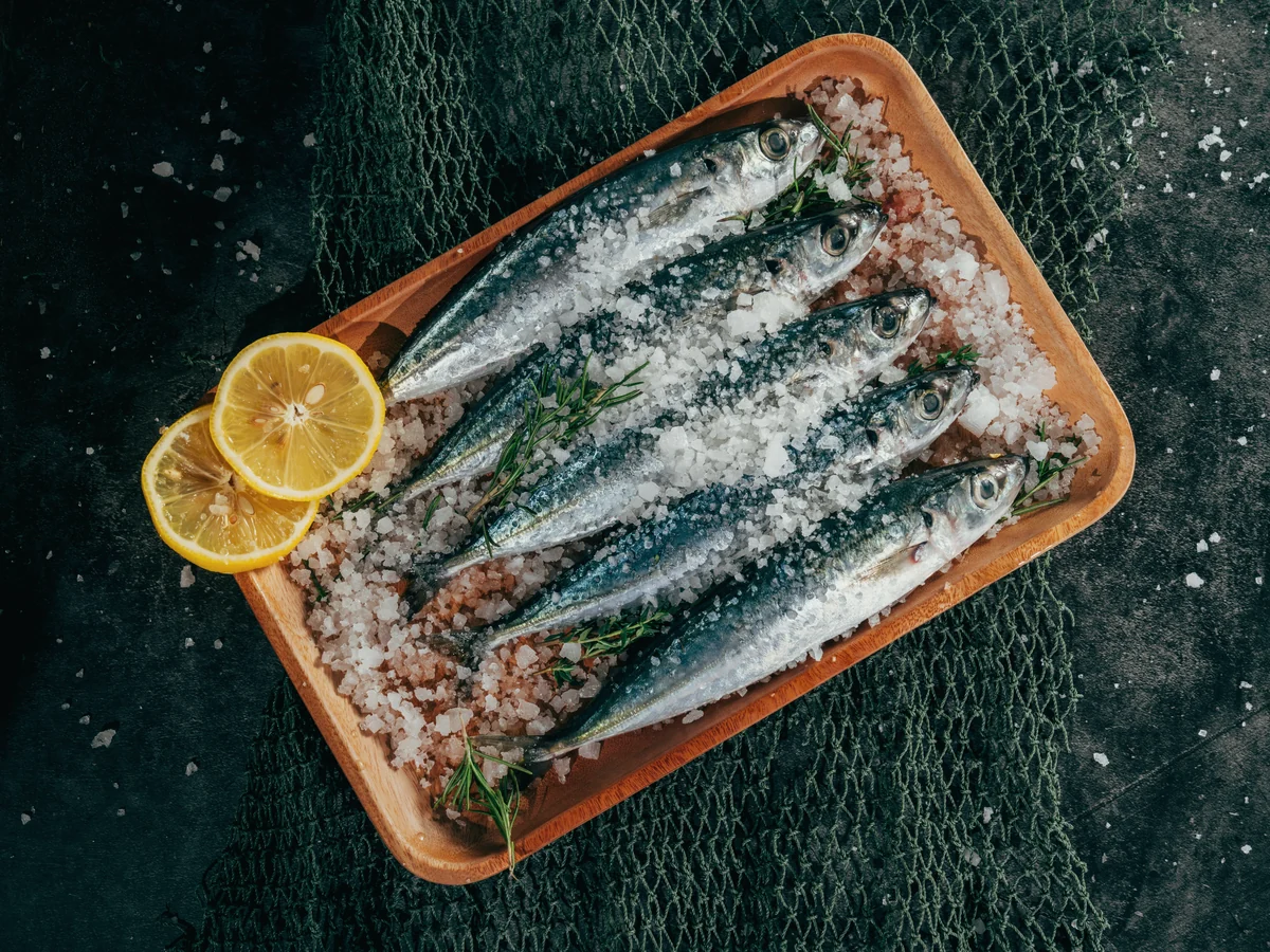 Alimentos con omega 3: sardinas frescas sobre sal gruesa en una bandeja de madera, con medio limón