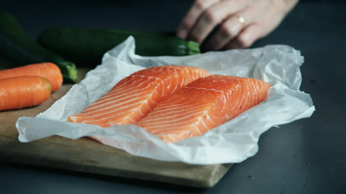 Dos lomos de salmón crudo sobre papel de horno, con zanahorias y un calabacín al fondo