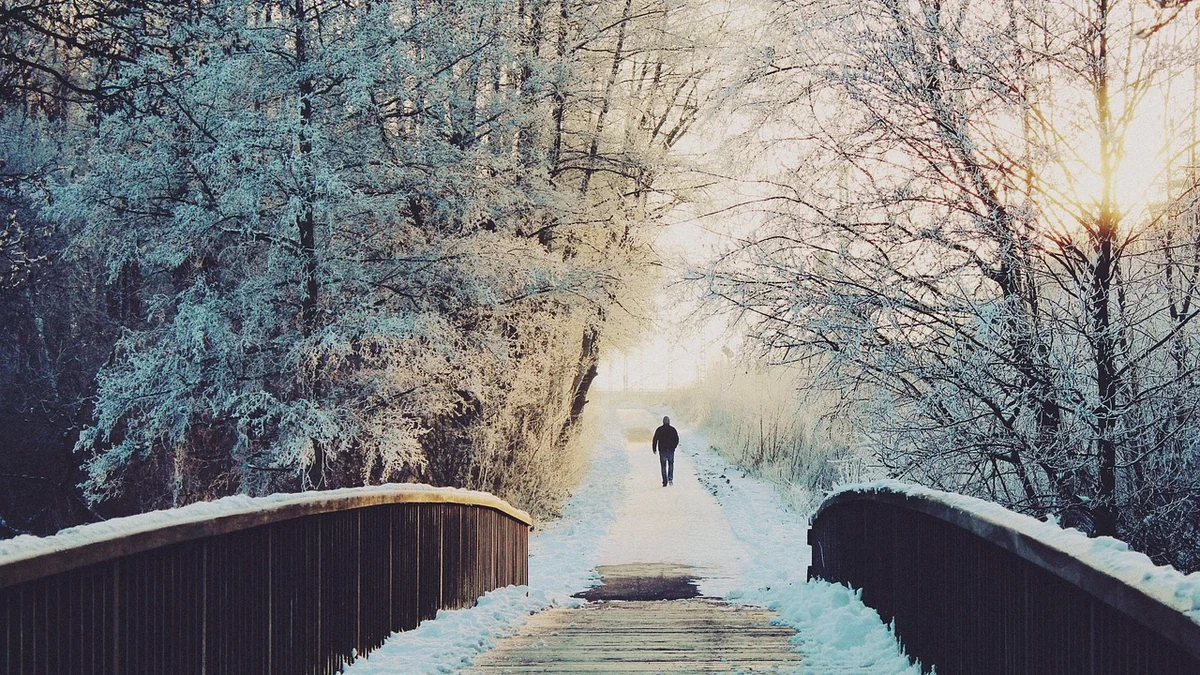 Persona caminando sola por un puente nevado con luz baja de invierno