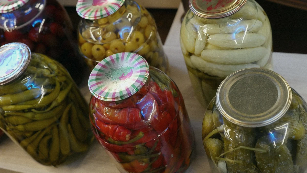 Tarros de cristal con conservas caseras de pimiento, pepinillo y fruta, cerrados y alineados sobre una mesa de madera