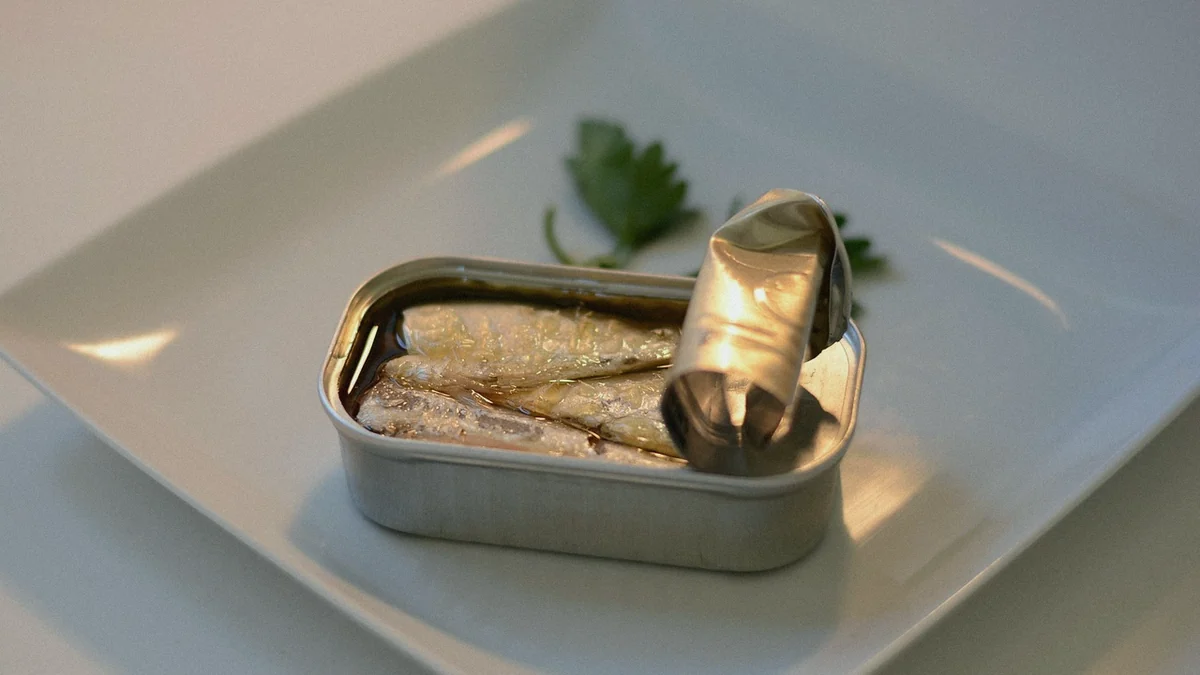 Lata de sardinas abierta sobre un plato blanco, con la tapa enrollada hacia atrás