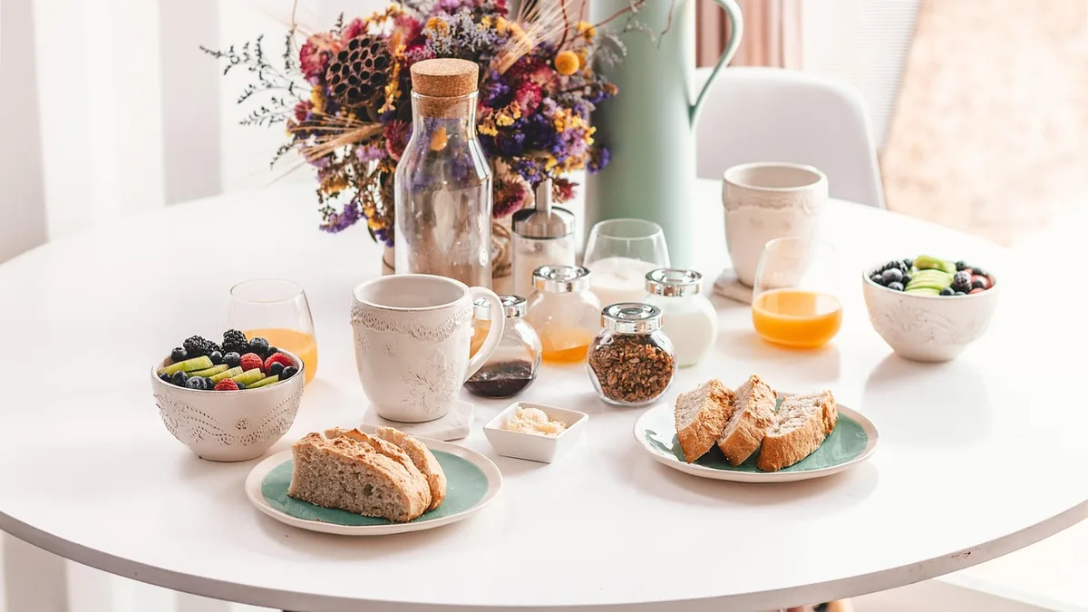 Mesa de desayuno vista desde arriba, con cuencos, fruta y bollería