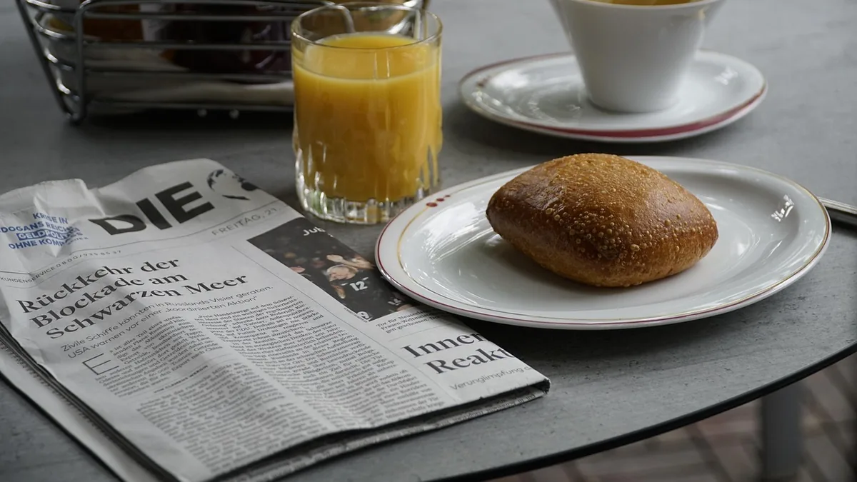 Desayuno con zumo, café y pan sobre una mesa, junto a un periódico
