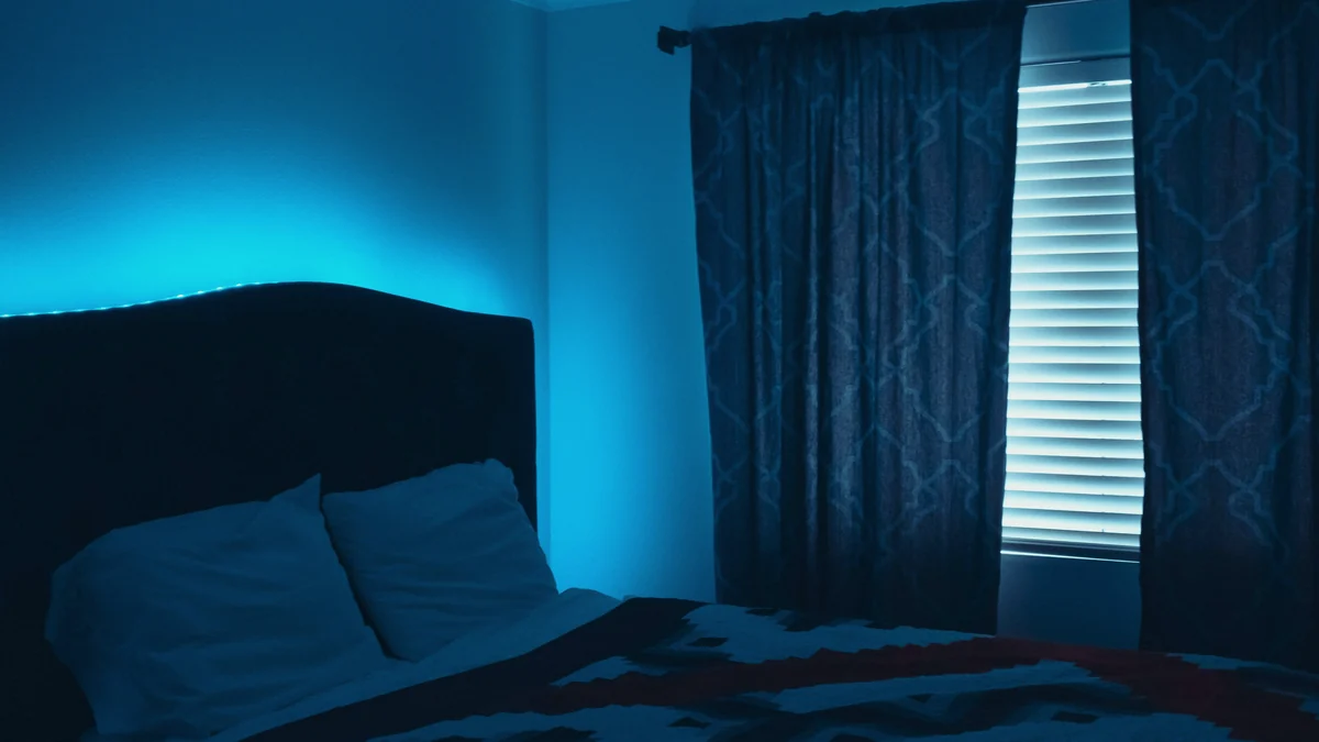 Dormitorio a oscuras por la noche, con la cama en penumbra y luz azulada junto a la cortina
