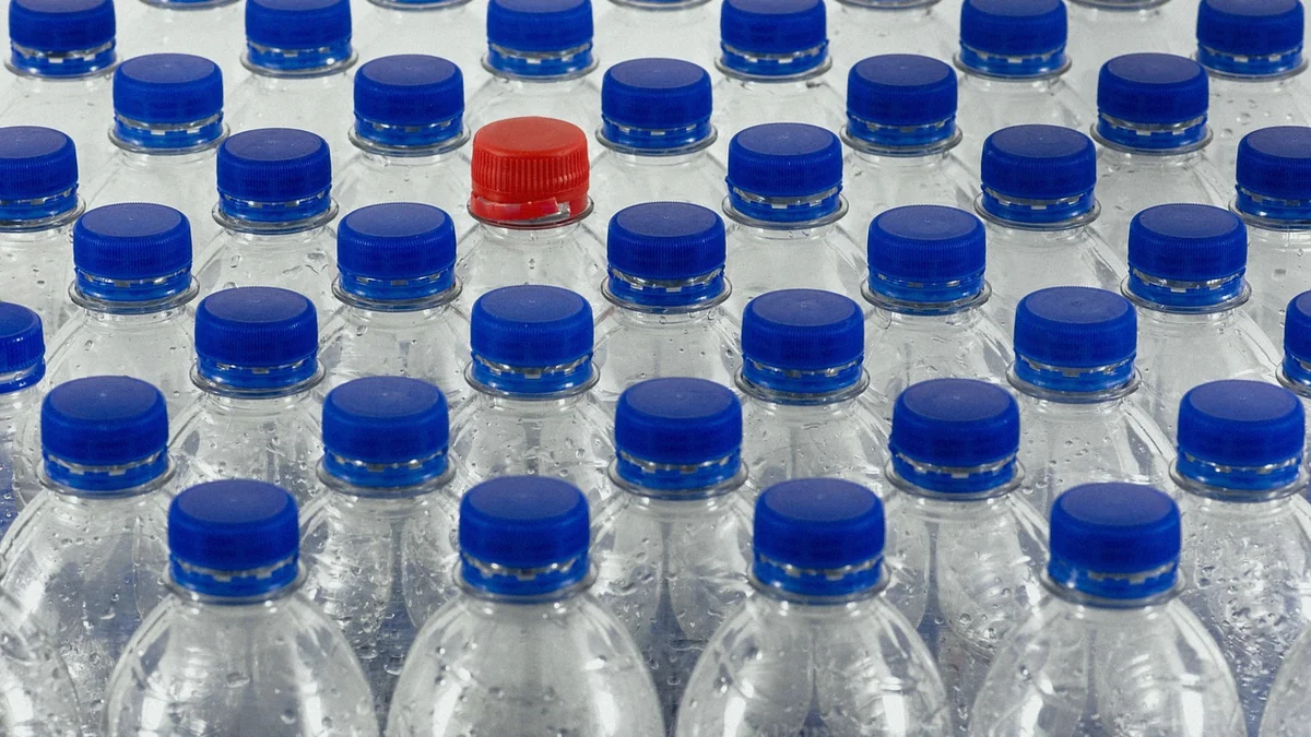 Filas de botellas de agua de plástico con el tapón azul y una con el tapón rojo