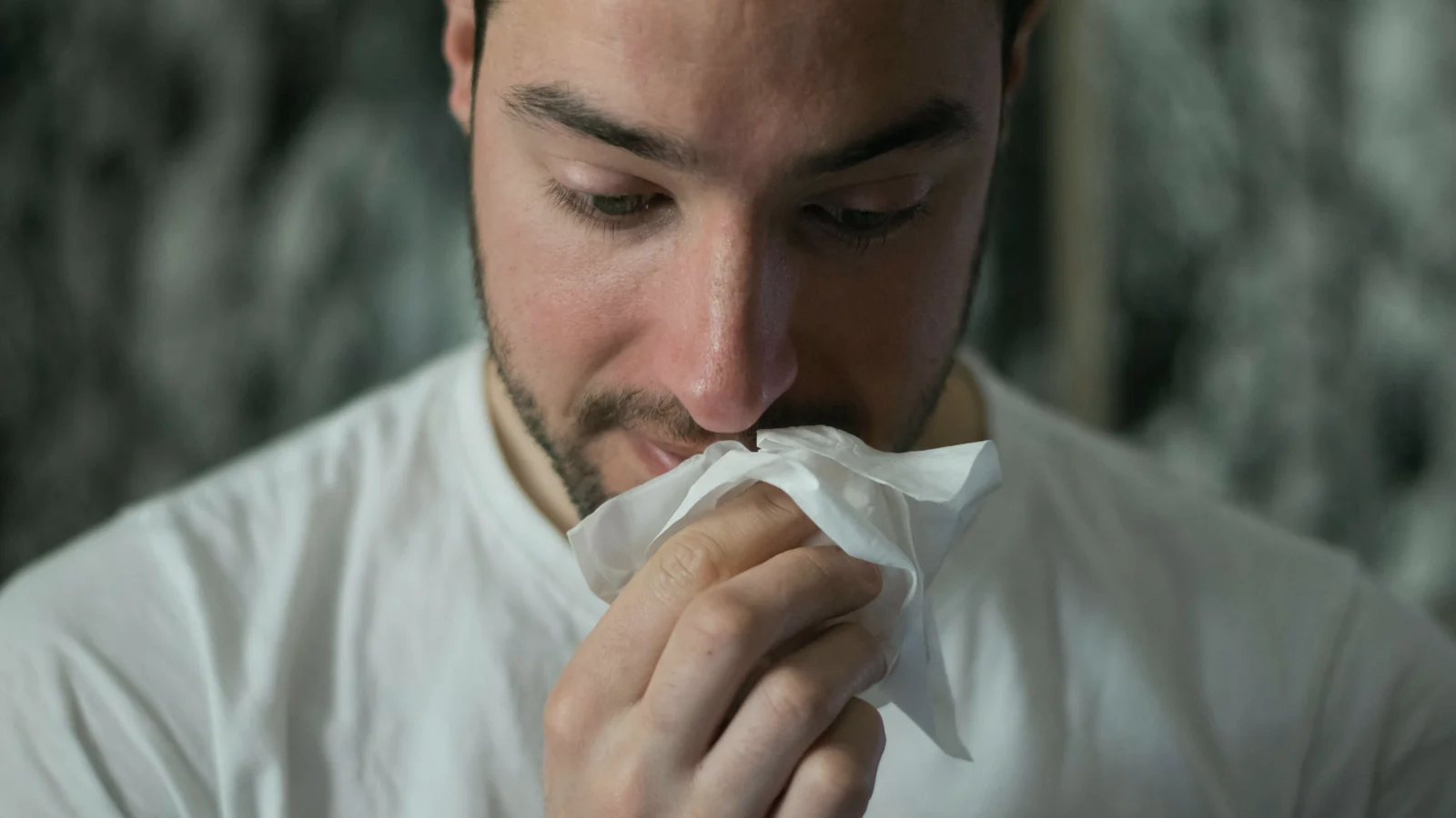 Hombre con camiseta blanca sonándose la nariz con un pañuelo de papel
