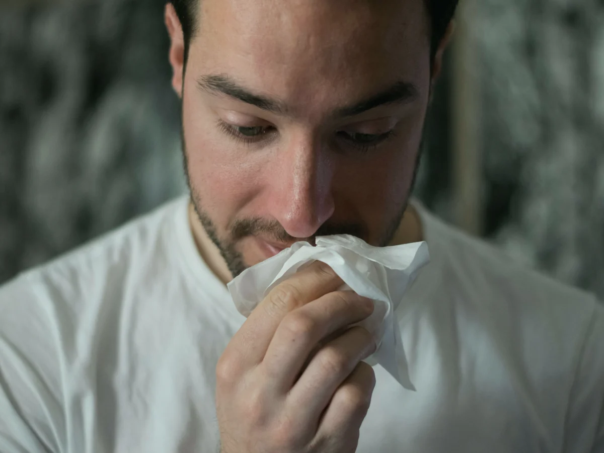 Hombre con camiseta blanca sonándose la nariz con un pañuelo de papel