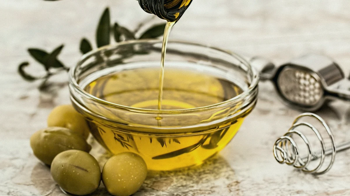 Aceite de oliva cayendo de la botella en un cuenco de cristal, con aceitunas al lado