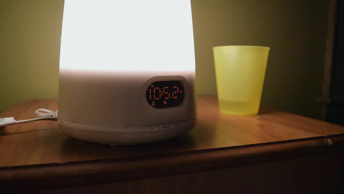Despertador con luz encendida sobre una mesilla de noche, junto a un vaso