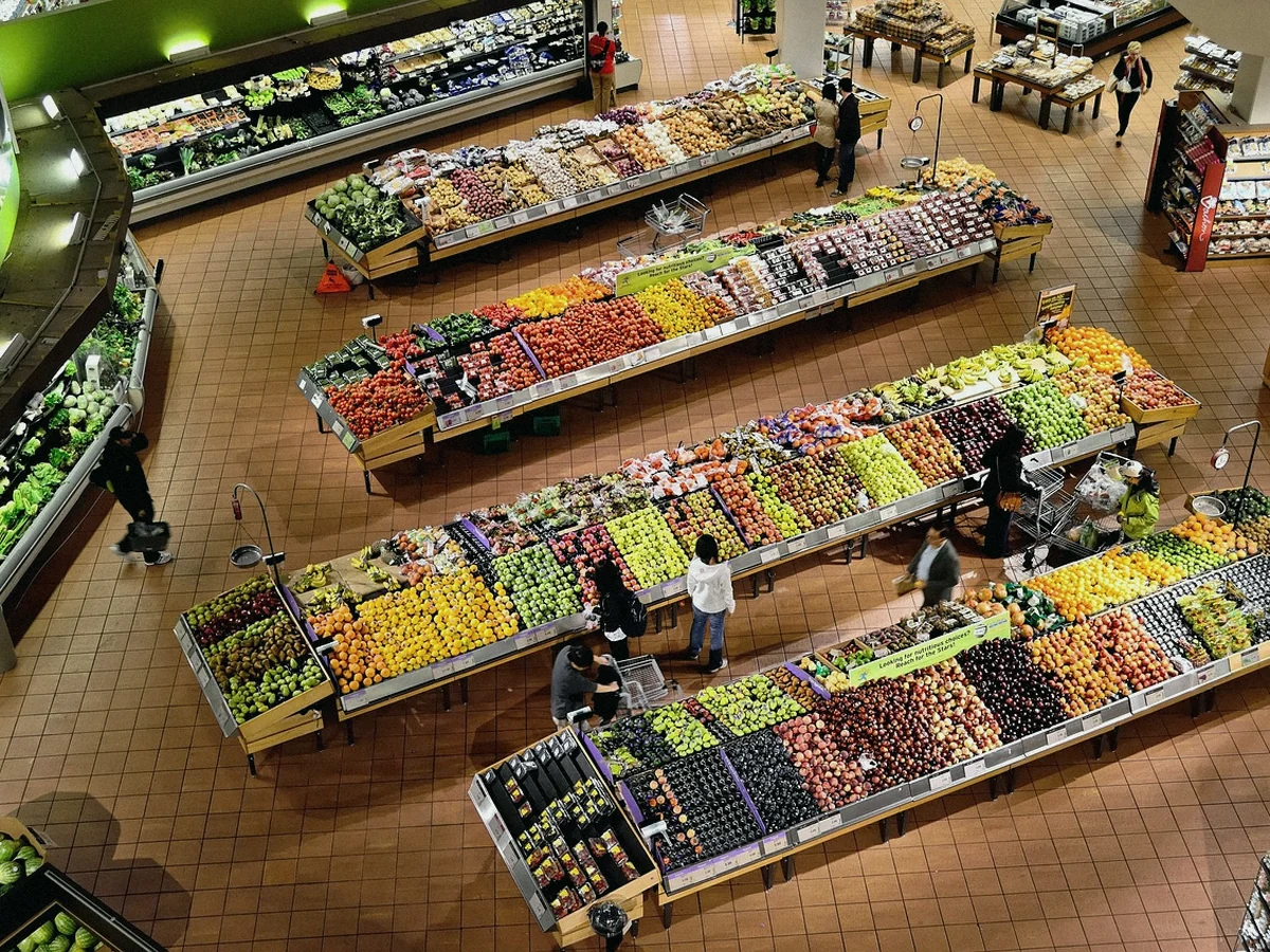 Sección de fruta y verdura de un supermercado vista desde arriba, con varias personas comprando entre los expositores