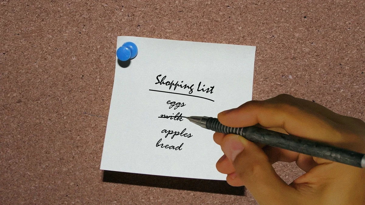 Una mano escribiendo a mano una lista de la compra en una libreta